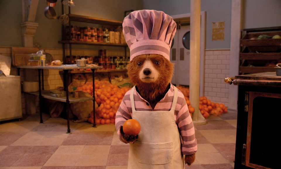 a bear wearing a chef 's hat and apron holds an orange
