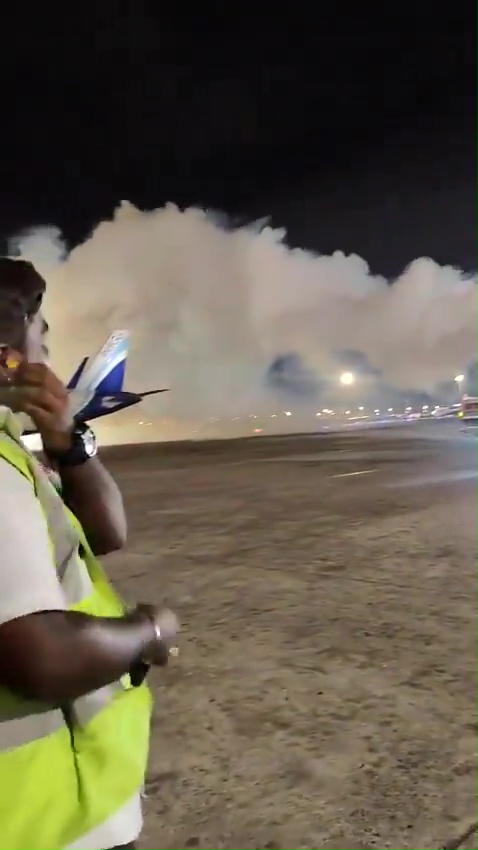 a man in a yellow vest is standing in front of an airplane on a runway at night .