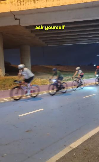 a group of people are riding bicycles down a road at night under a bridge .