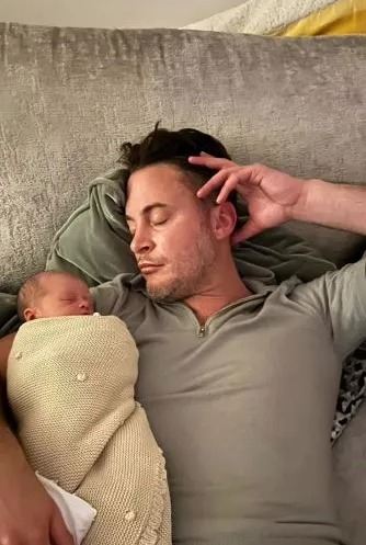 a man is sleeping with a newborn baby wrapped in a blanket .