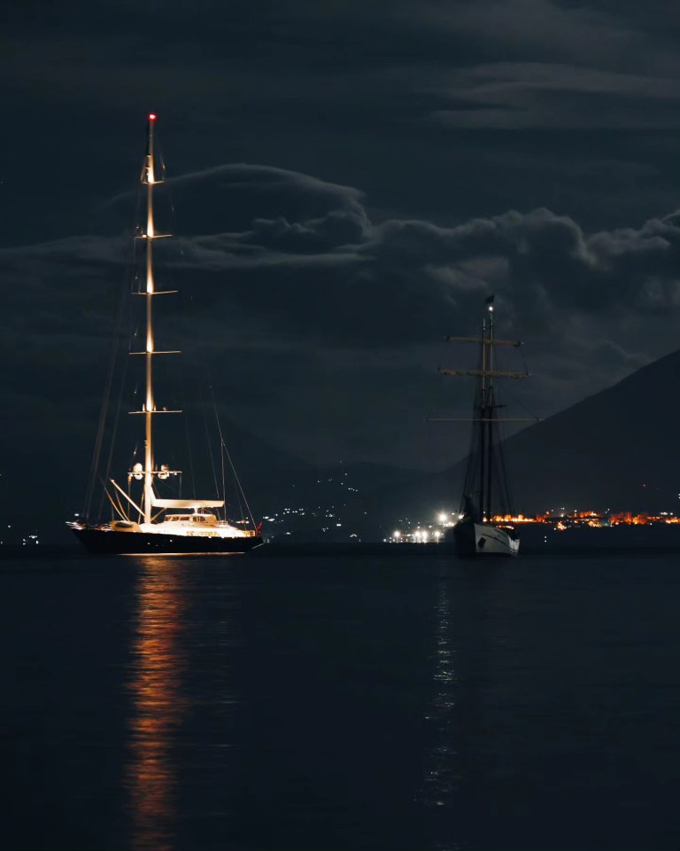 two sailboats are in the water at night with mountains in the background