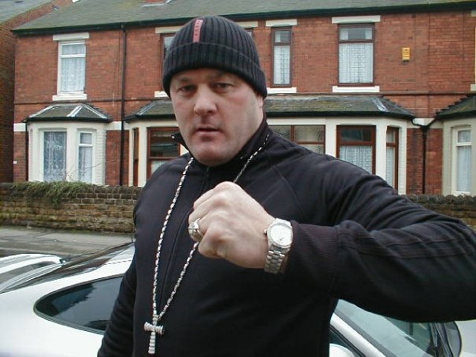a man wearing a beanie and a watch stands in front of a brick house