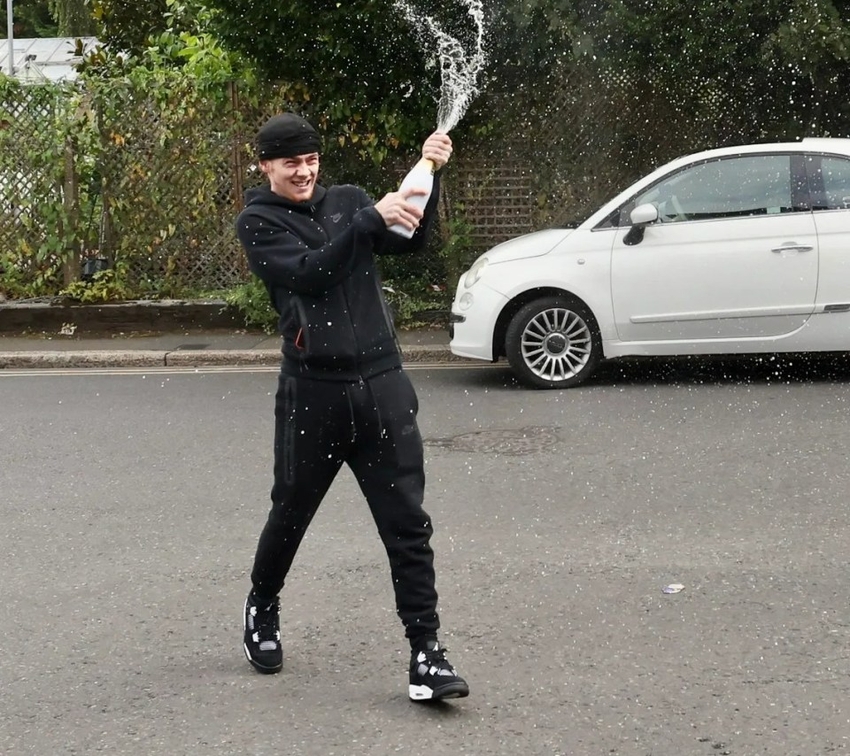 a man is holding a bottle of champagne in front of a white car