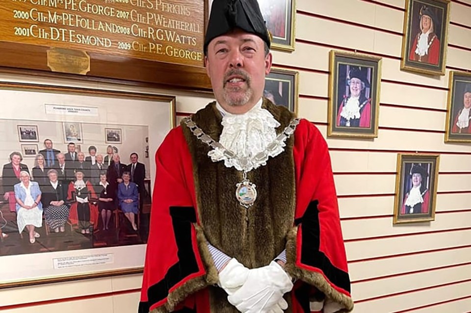 a man in a mayor 's robe stands in front of a wall of pictures
