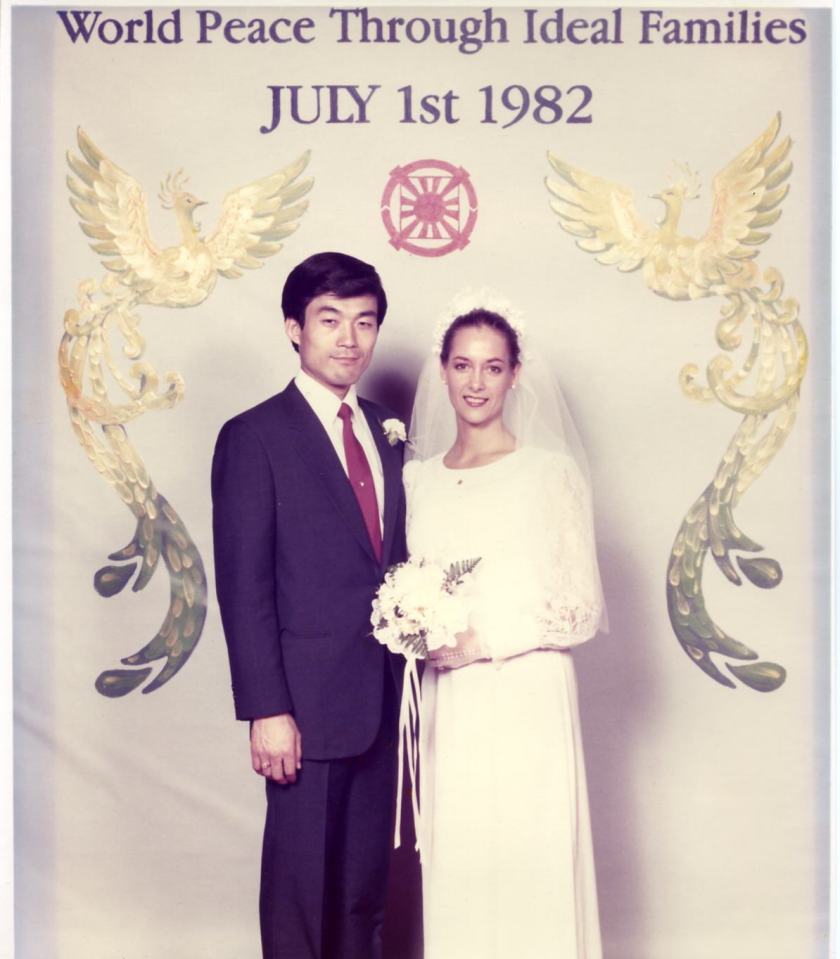 a bride and groom pose in front of a sign that says world peace through ideal families