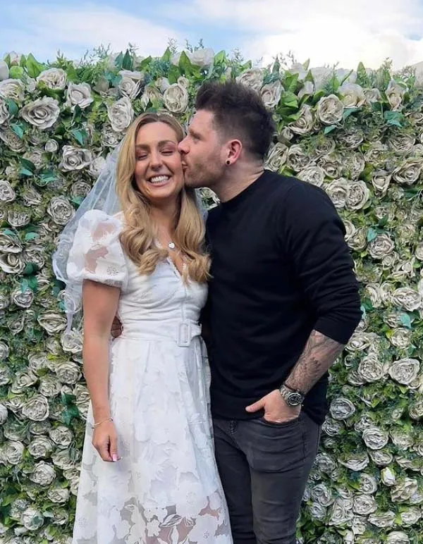 a man kisses a woman on the cheek in front of a wall of flowers .