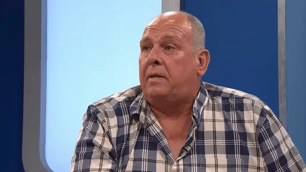 a man in a plaid shirt is sitting in front of a blue wall .