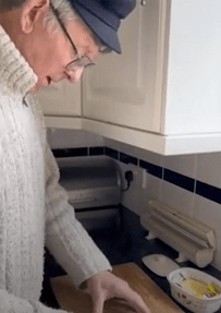 an elderly man is cutting vegetables on a cutting board in a kitchen .