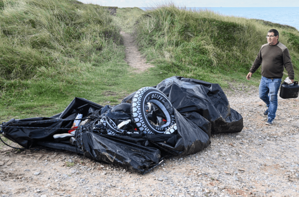 a man carrying a canister walks past a pile of garbage including a tire that says octane on it
