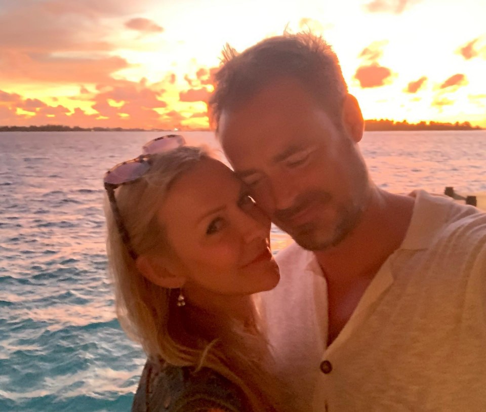 a man and woman are posing for a picture in front of the ocean at sunset