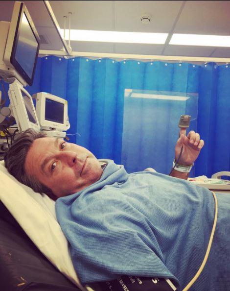 a man is laying in a hospital bed holding a remote control