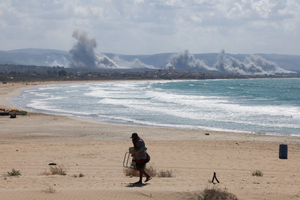 a man walking on a beach with smoke coming out of the mountains in the background