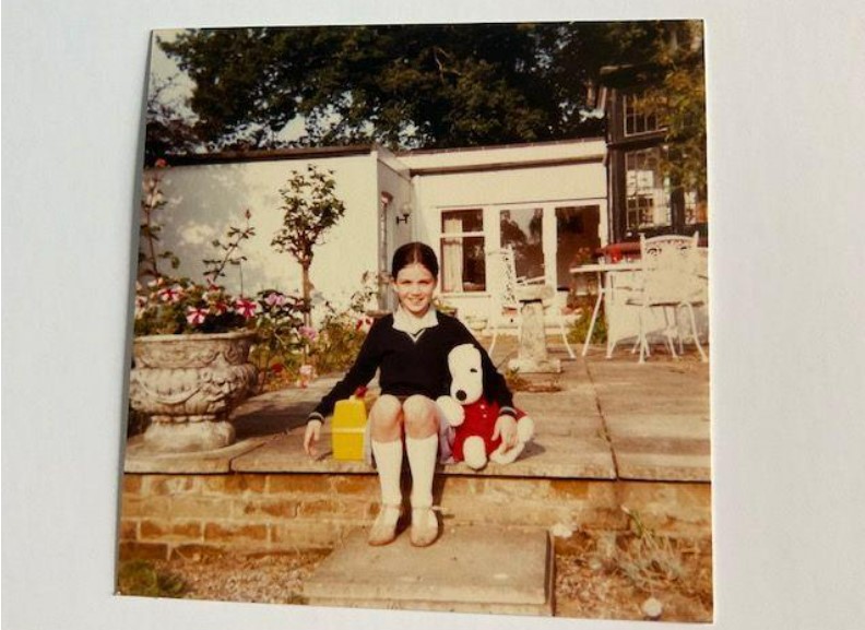 a little girl sits on a brick step holding a stuffed snoopy