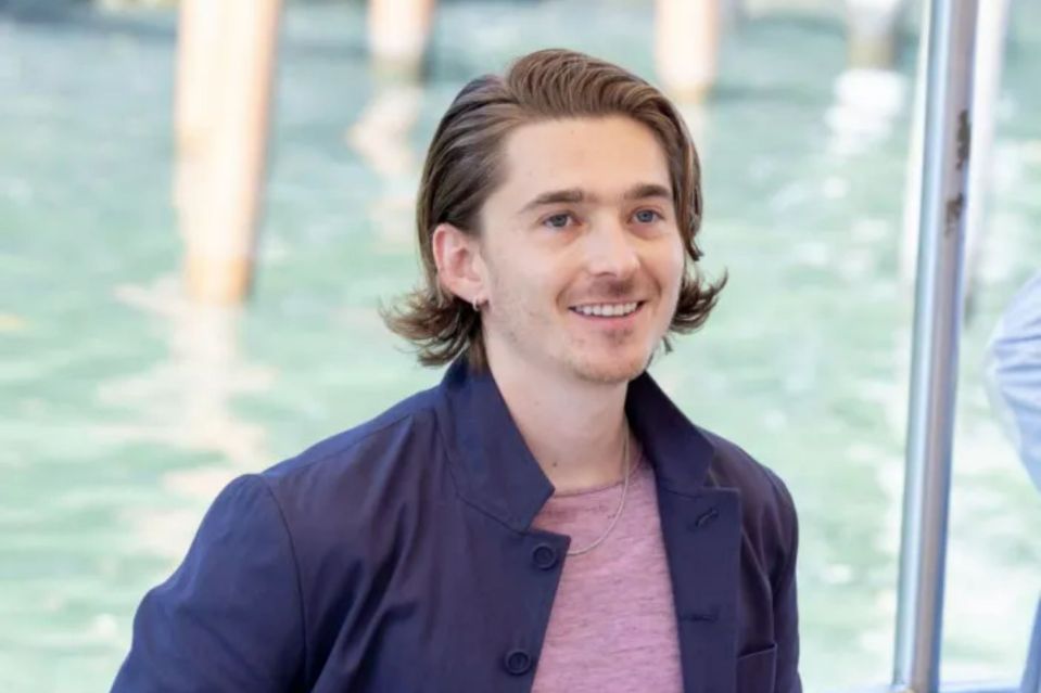 a man wearing a blue jacket and a pink shirt smiles for the camera