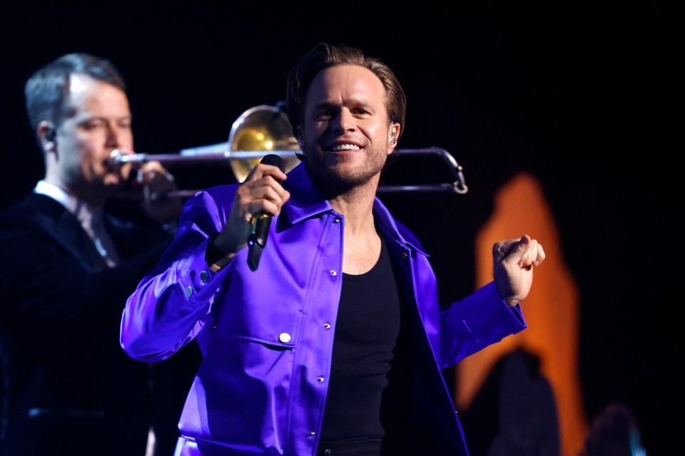 a man in a purple jacket is singing into a microphone