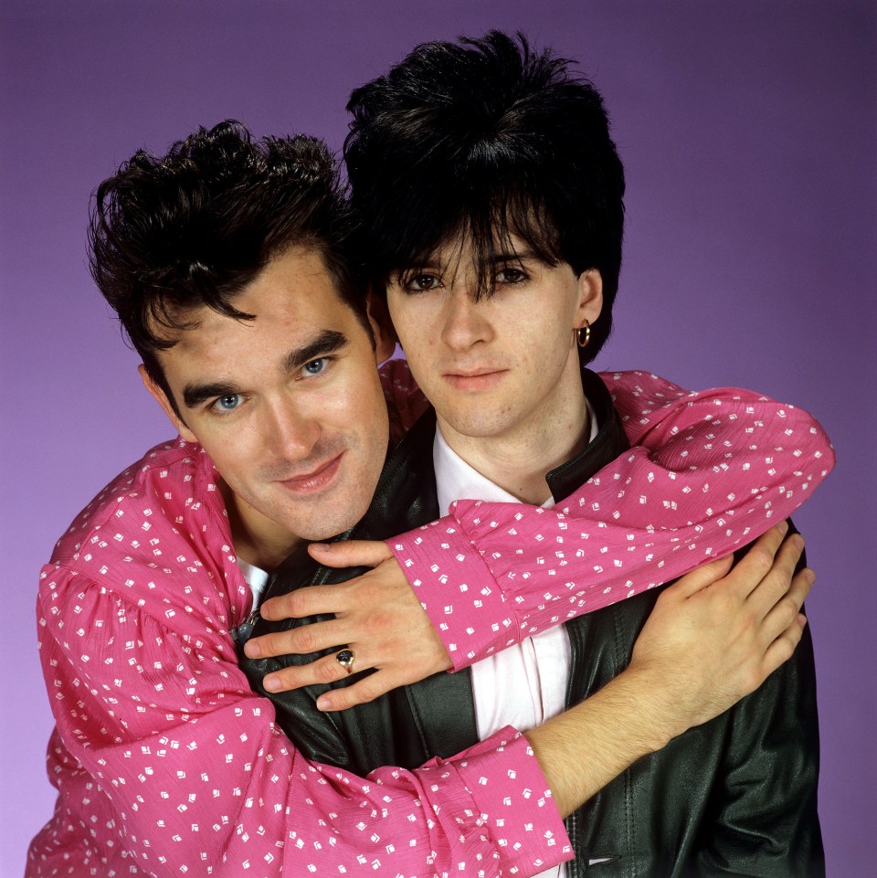 a man in a pink shirt is hugging another man in a black jacket