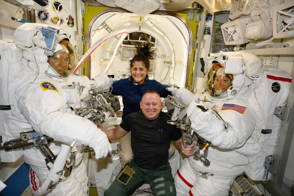 a man in a black under armour shirt poses with two other astronauts