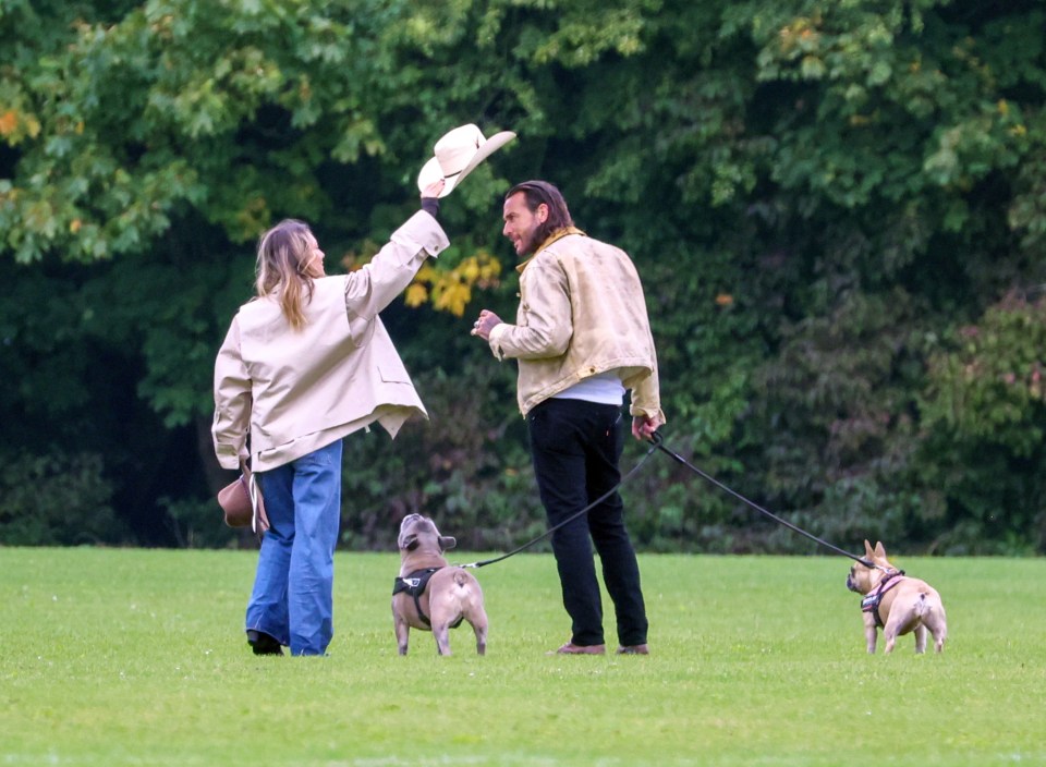 a woman throws a hat in the air while walking two dogs