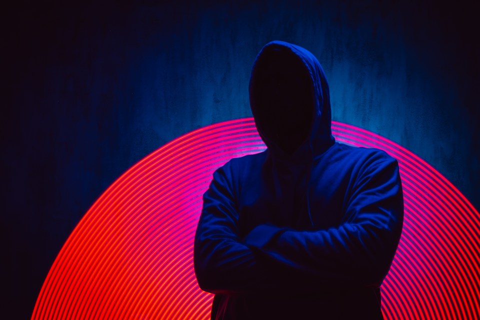 a man in a blue hoodie stands with his arms crossed