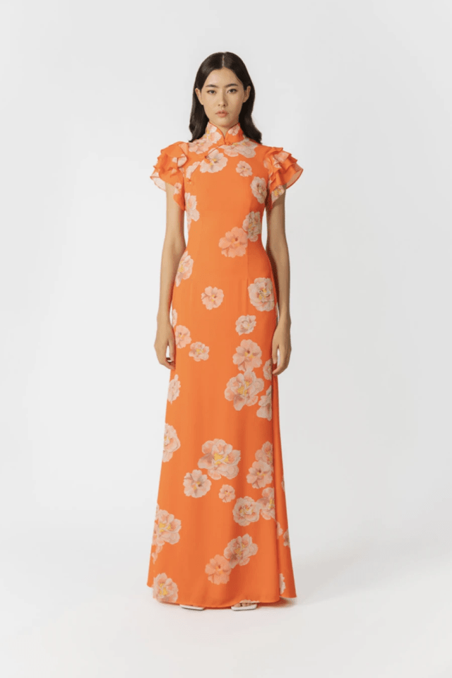 a woman is wearing a long orange dress with white flowers on it