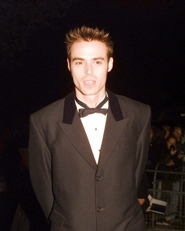 a man in a tuxedo and bow tie stands in front of a crowd