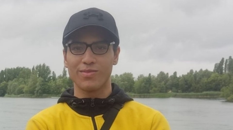 a young man wearing a black under armour hat stands in front of a lake
