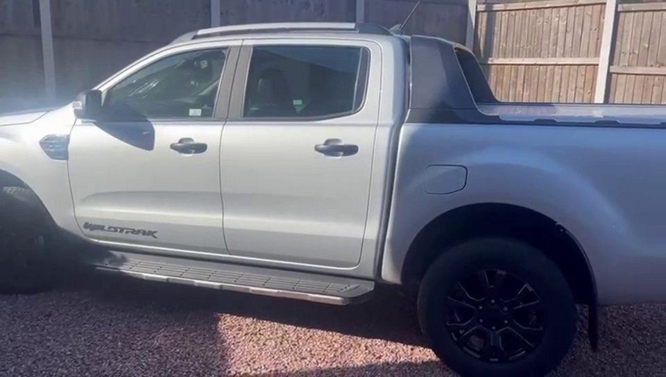 a white ford wildtrak truck is parked in front of a wooden fence