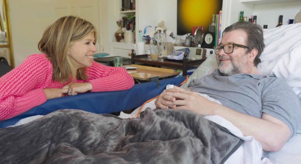 a woman in a pink sweater talks to a man in a hospital bed