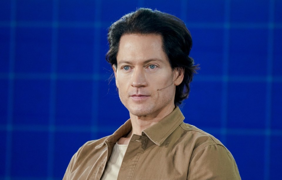 a man in a brown shirt stands in front of a blue background