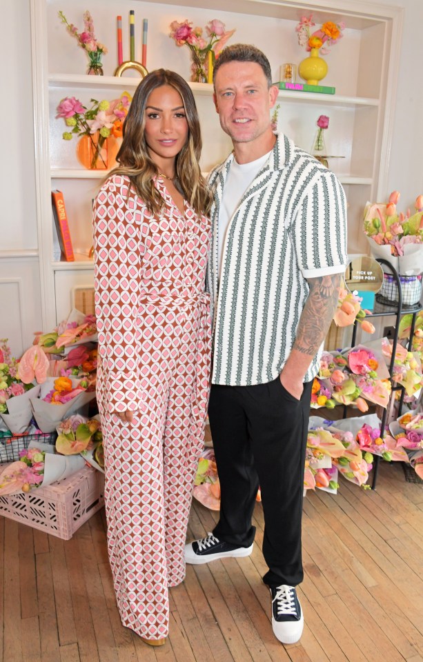 a man and a woman pose for a picture in front of flowers