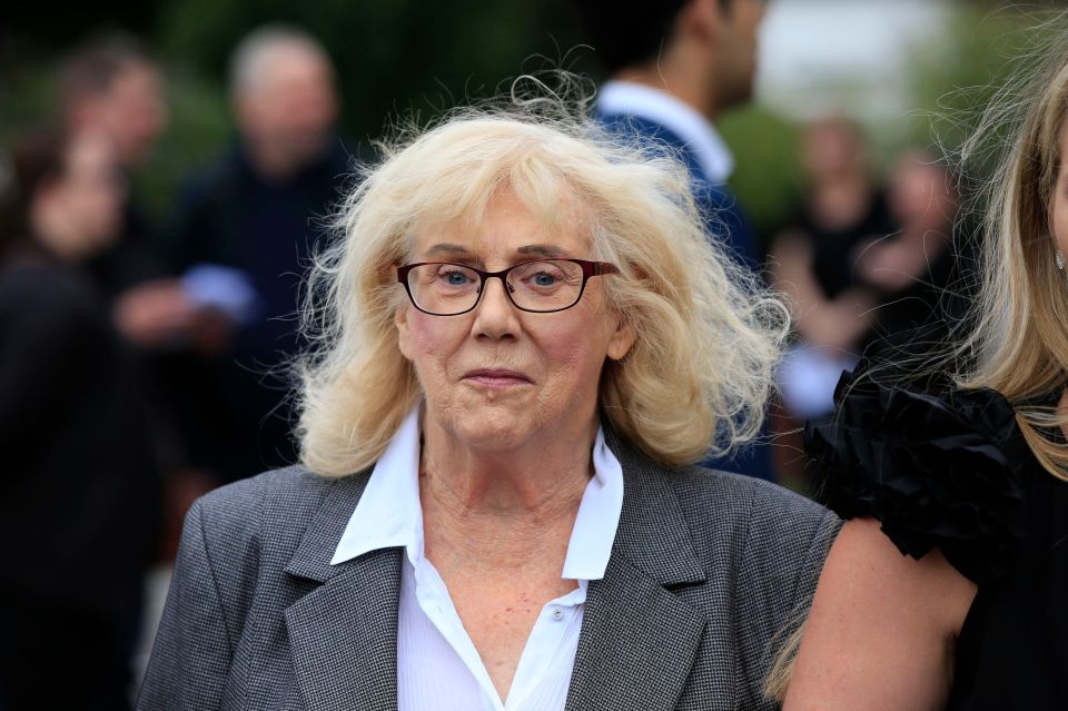 a woman with blonde hair wearing glasses and a grey jacket