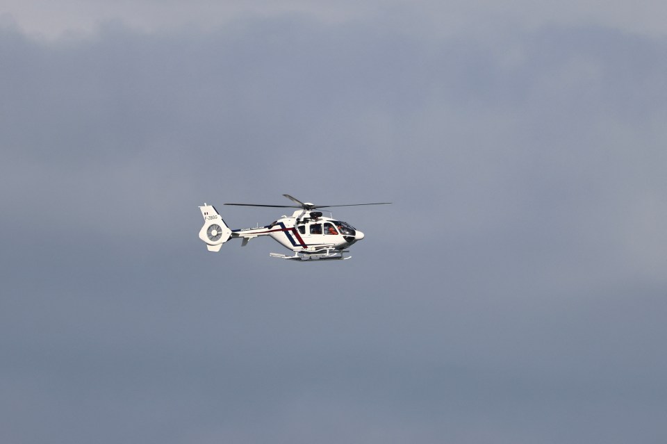 a white helicopter with a red stripe on the tail is flying in the sky