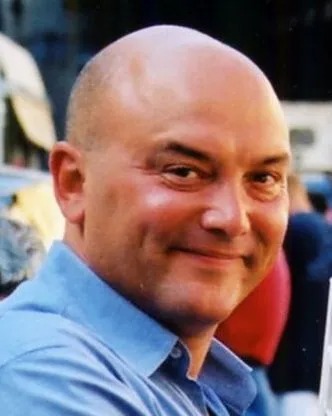 a bald man in a blue shirt is smiling for the camera