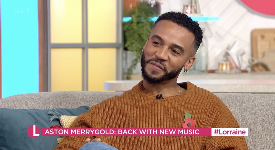 a man in a brown sweater sits on a couch on a television show