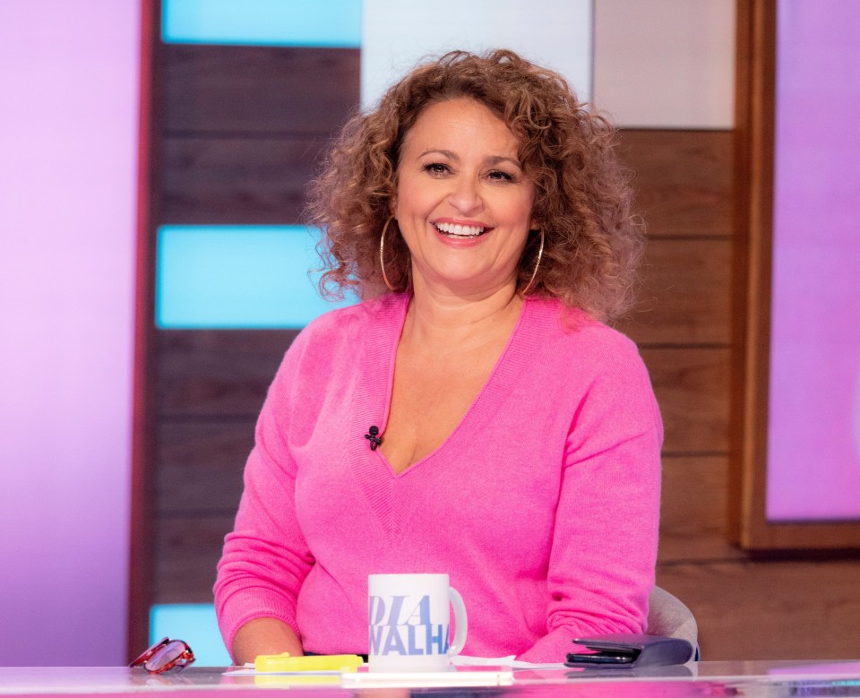 a woman in a pink sweater sits at a table with a mug that says ' aloha ' on it
