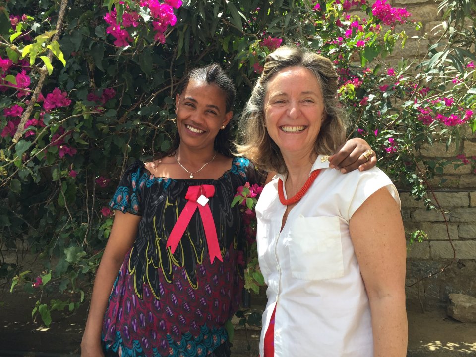 two women are posing for a picture in front of a bush with pink flowers