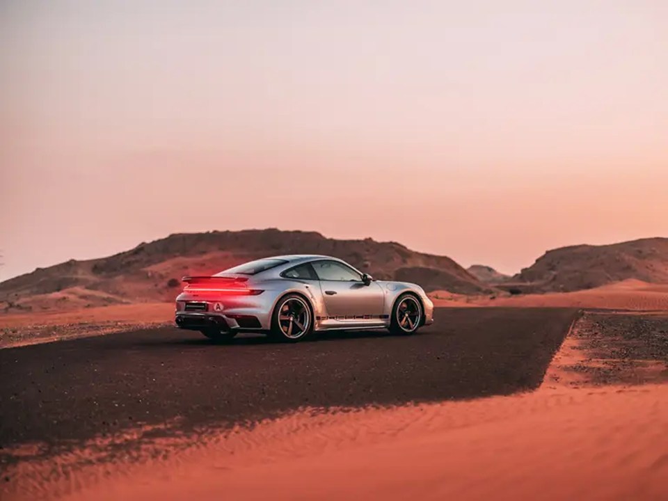 a silver porsche is driving down a desert road