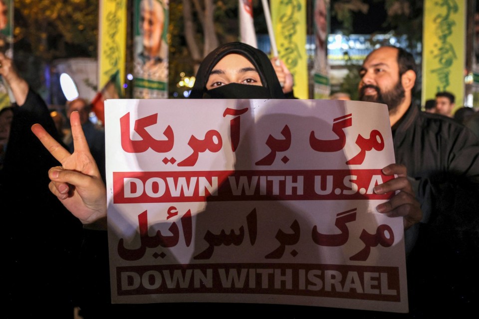 A woman holds a sign denouncing the US and Israel during a rally celebrating after Iran launched a barrage of missiles at Israel in response to the killings of Hezbollah's leader Hassan Nasrallah and other Iran-backed militants outside Imam Jaafar Sadiq Mosque in Tehran's Palestine Square on October 1, 2024. Reports said Iran fired between 150 and 200 missiles in the attack, the country's second on Israel after a missile and drone attack in April in response to a deadly Israeli air strike on the Iranian consulate in Damascus. (Photo by ATTA KENARE / AFP) (Photo by ATTA KENARE/AFP via Getty Images)