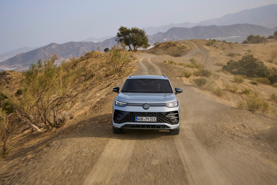 a volkswagen is driving down a dirt road with mountains in the background