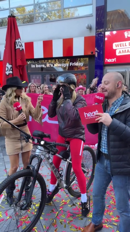 a woman wearing a helmet stands next to a man holding a heart sign