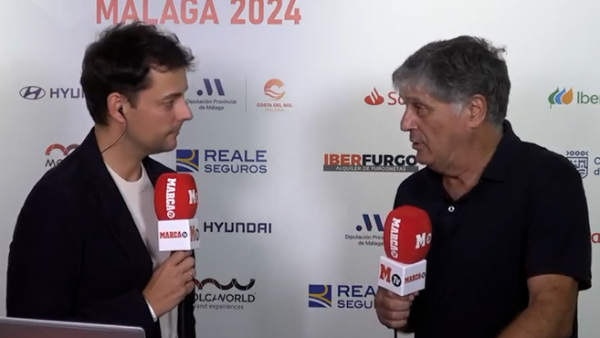 two men are talking in front of a wall that says malaga 2024