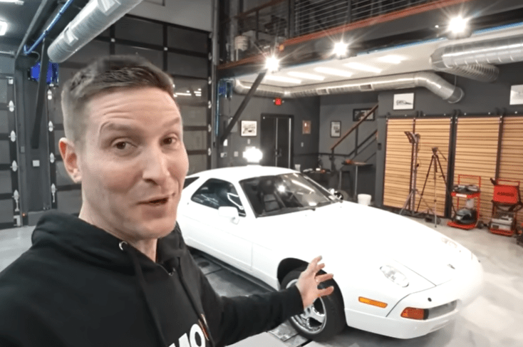 a man wearing a black hoodie with the word mo on it stands in front of a white car