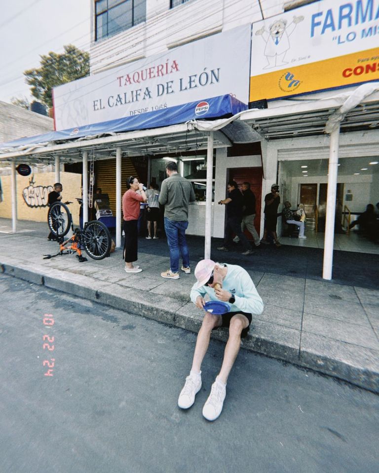 a man sits on the sidewalk in front of a taqueria