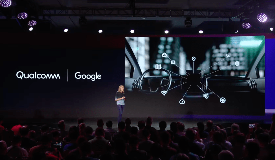 a woman stands on a stage in front of a screen that says qualcomm and google