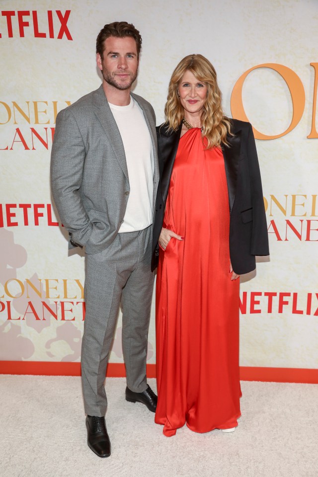 a man in a suit and a woman in a red dress pose on a red carpet with a netflix sign behind them