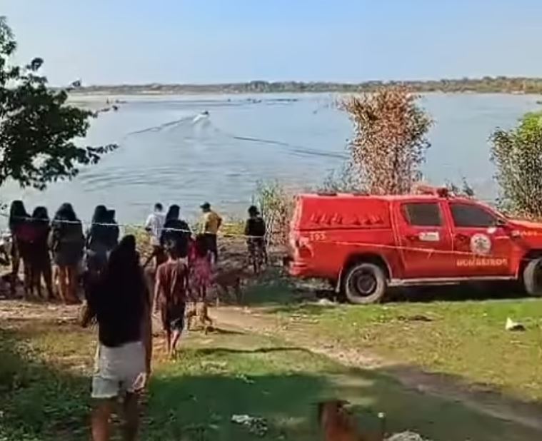 a group of people are standing on the shore of a lake next to a red truck .