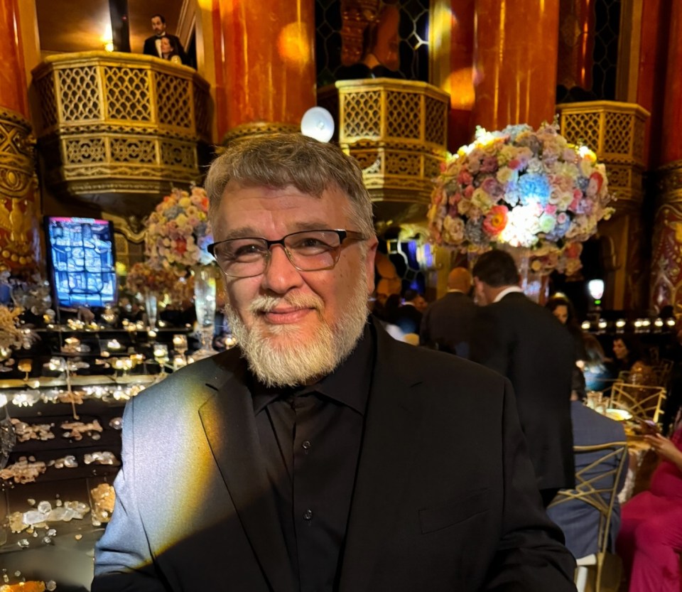 a man with glasses and a beard stands in front of flowers