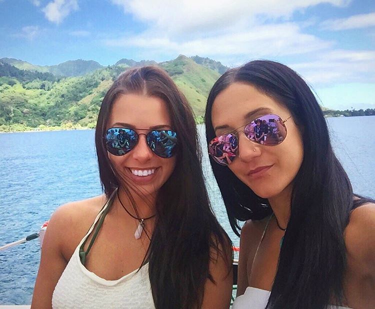two women wearing sunglasses are standing next to each other in front of a body of water