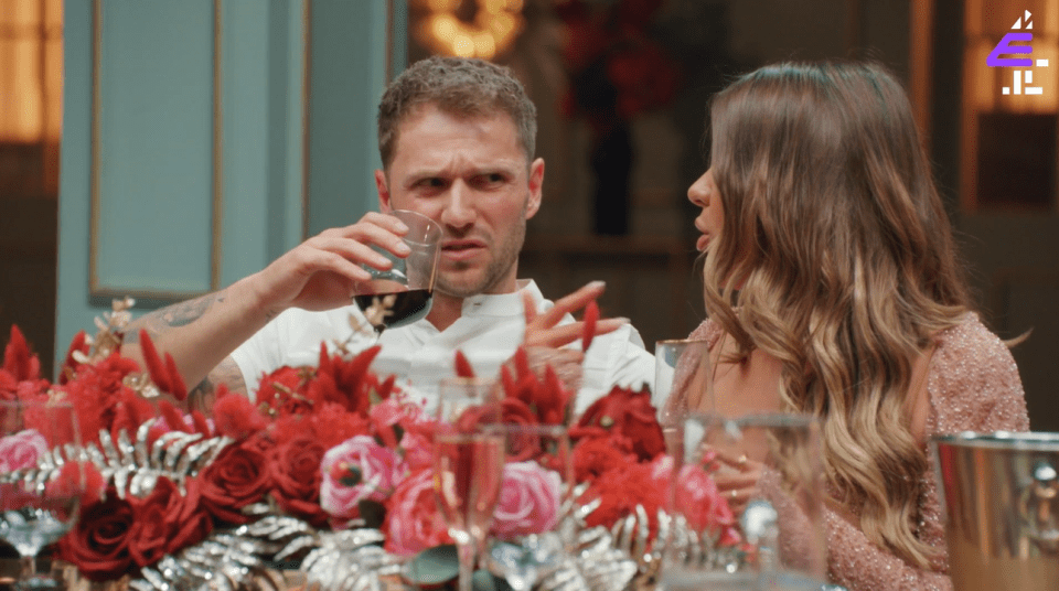 a man and a woman are sitting at a table with flowers and a purple e in the corner