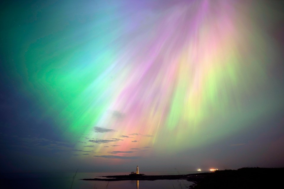 the aurora borealis shines brightly in the night sky over a lighthouse